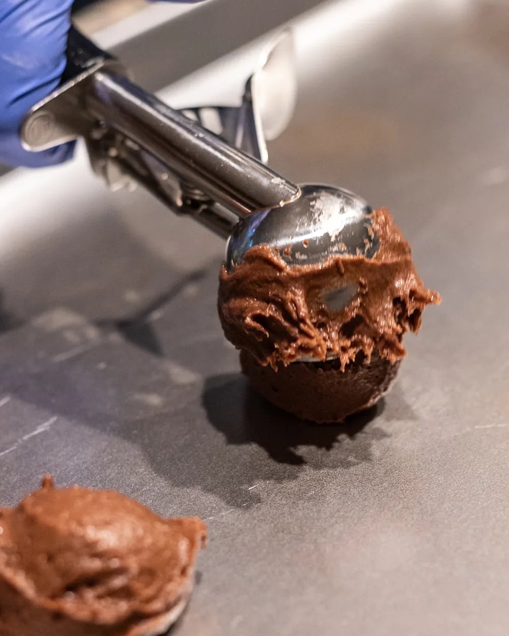 A scoop portioning brownie batter onto a baking tray.