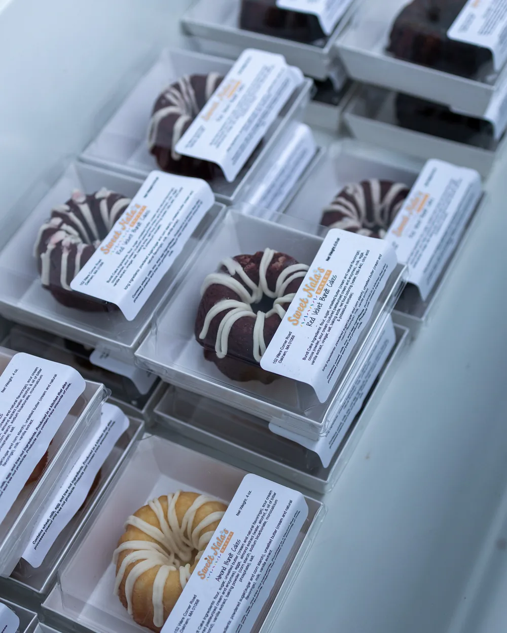 Individually boxed mini bundt cakes with printed flavor labels, lined up in the cart's case.