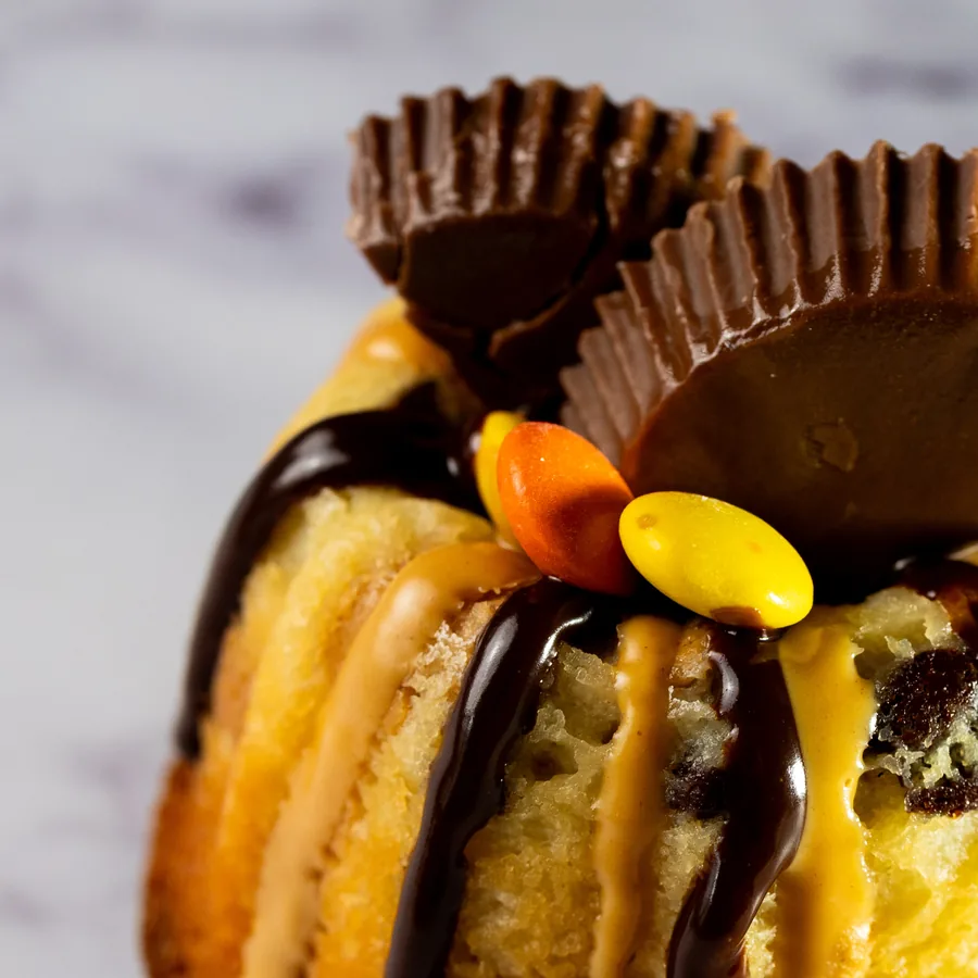 A mini bundt cake topped with peanut butter cups, Reese's Pieces and chocolate drizzle.