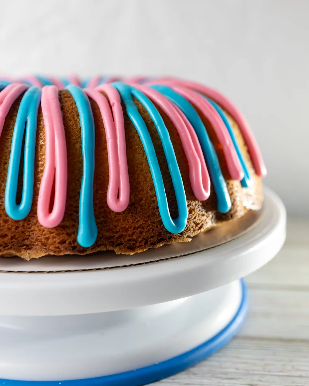 A full size bundt cake for a gender reveal, piped all over with alternating pink and blue icing, on a white cake stand.