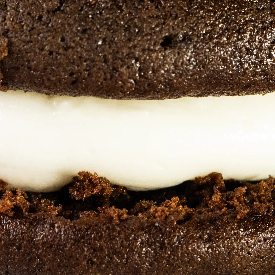 A whoopie pie cut open, showing two soft chocolate cakes around a thick layer of cream filling.